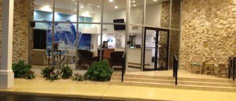 A hotel entrance with a stone facade, a reception desk, and a view of the interior through glass doors.