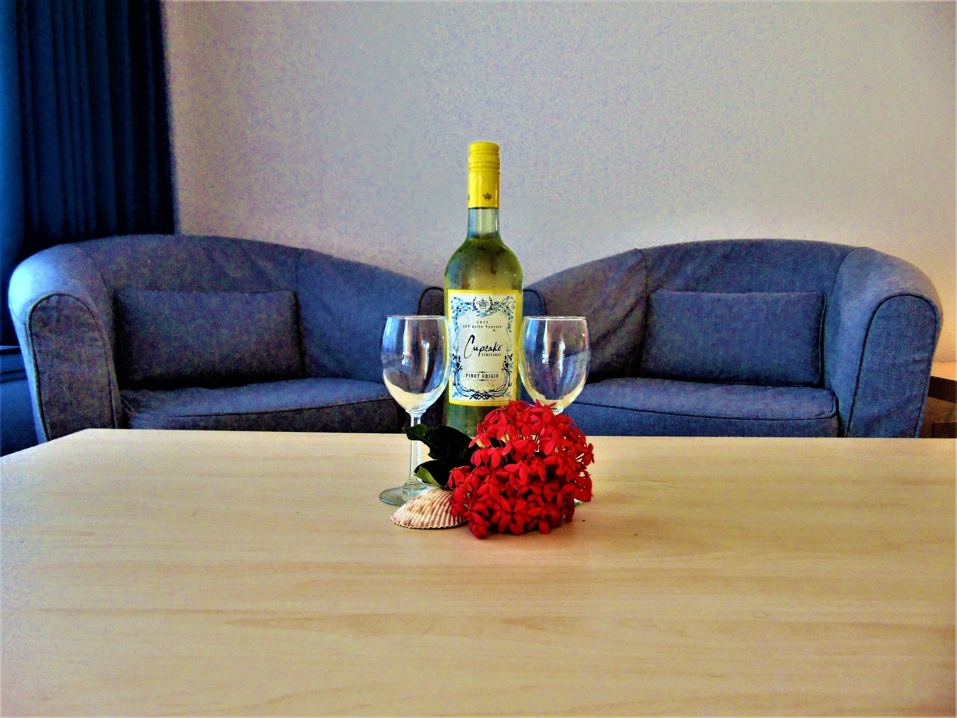 A table with a bottle of wine, two wine glasses, and a red flower arrangement.