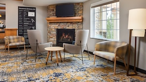 A cozy lounge area with a stone fireplace, comfortable seating, and a large window providing natural light.