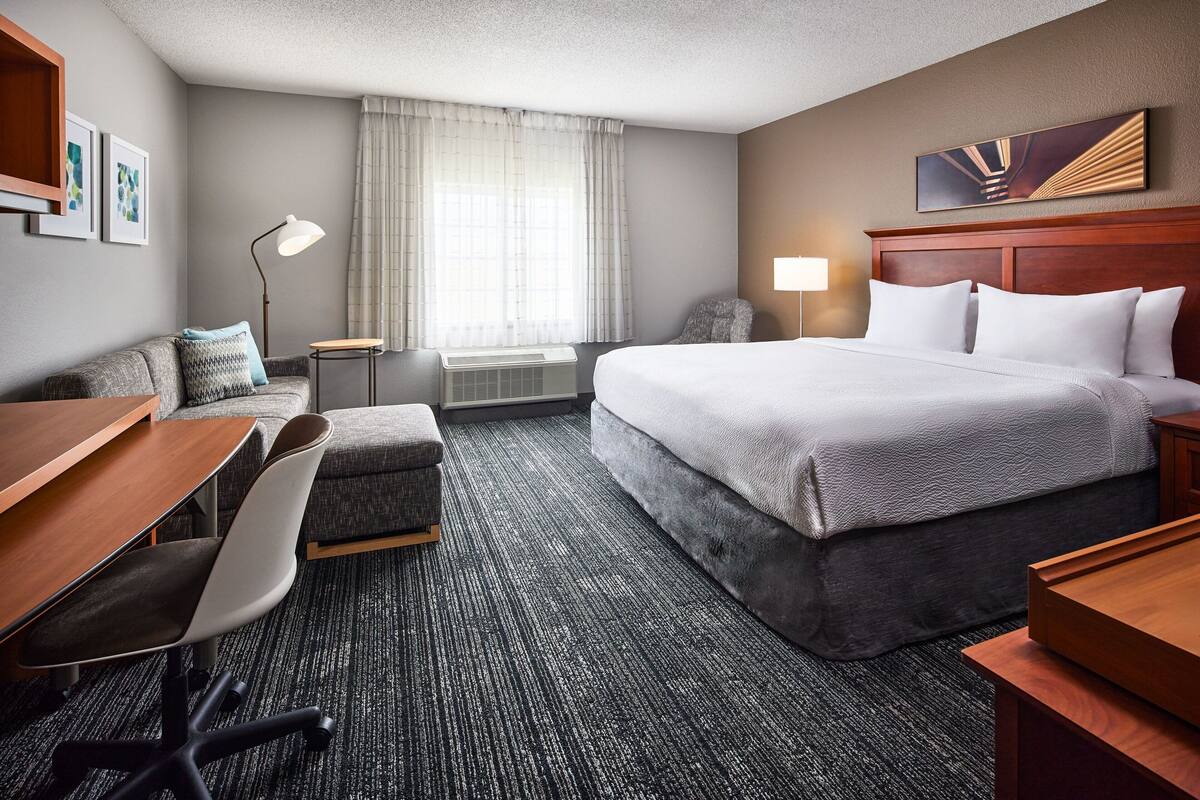 A hotel room with a bed, desk, chair, and a small table.