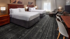A hotel room with two beds, a desk, a chair, and a television.