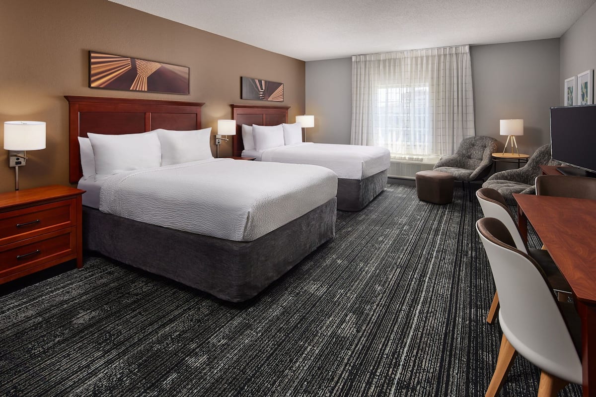A hotel room with two beds, a desk, a chair, and a television.