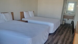Une chambre avec deux lits, un plancher en bois, une petite salle de bain avec un miroir et un bureau en bois.
