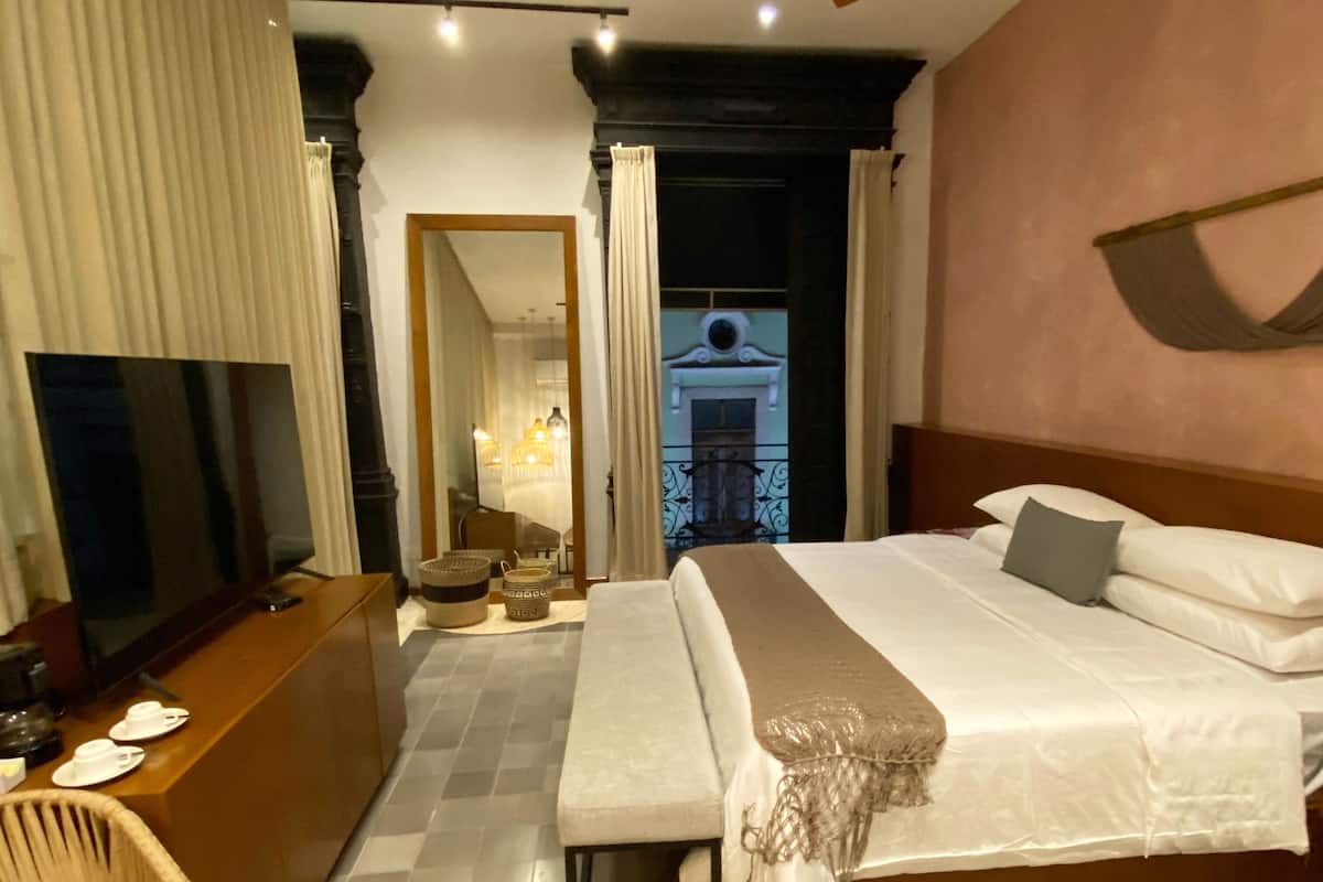 A hotel room with a large bed, a desk with a TV, a ceiling fan, and a balcony with a view.