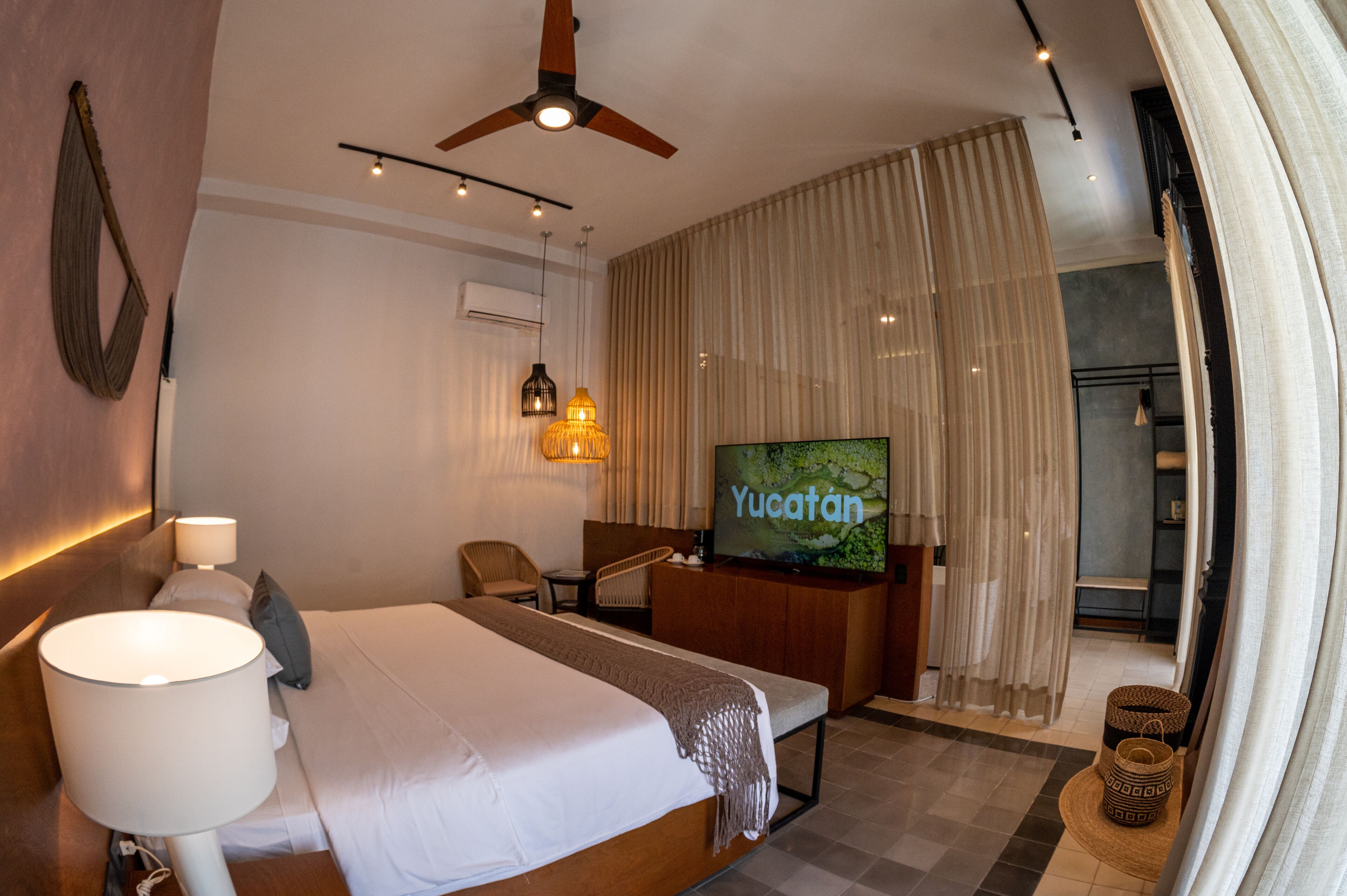 A hotel room with a bed, a desk, a television, and a ceiling fan.