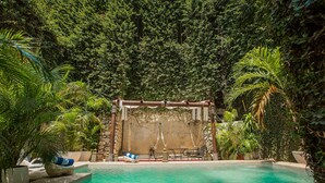A pool area with a stone wall, lounge chairs, and potted plants.