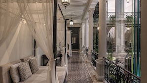 A luxurious bedroom with a canopy bed, a patterned floor, and a view of a garden through large windows.