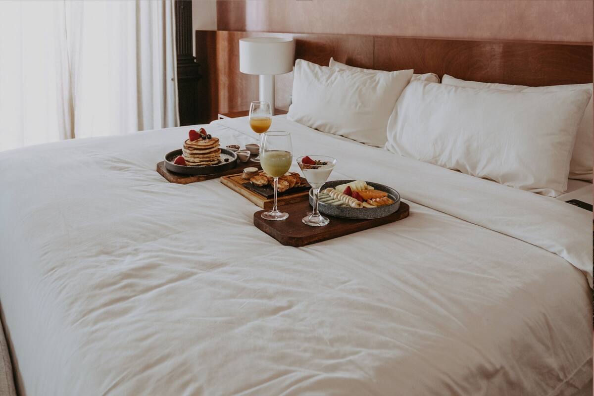 A neatly made bed with a breakfast tray featuring pancakes, fruit, and a glass of orange juice.