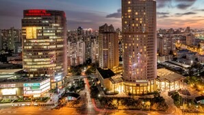A modern high-rise building with a prominent red sign at the top, surrounded by other tall buildings and a busy urban street at night. - Sheraton Grand Shanghai Pudong Hotel & Residences (Shanghai)
