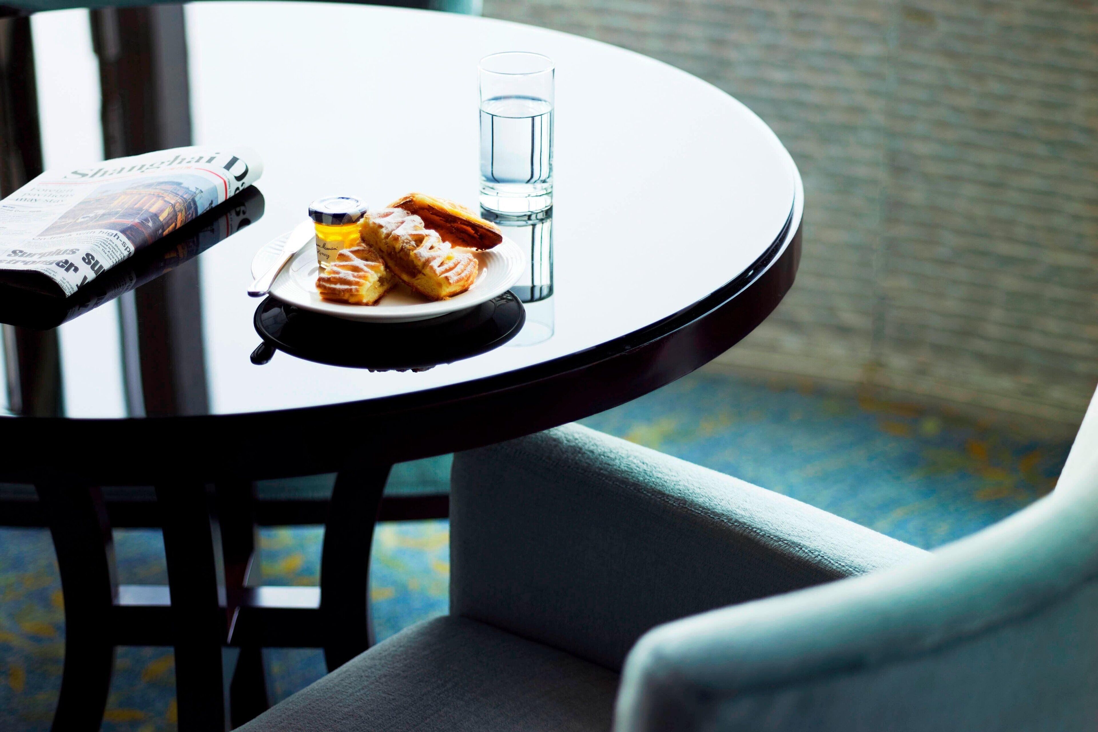 A round table with a newspaper, a plate with pastries, and a glass of water.