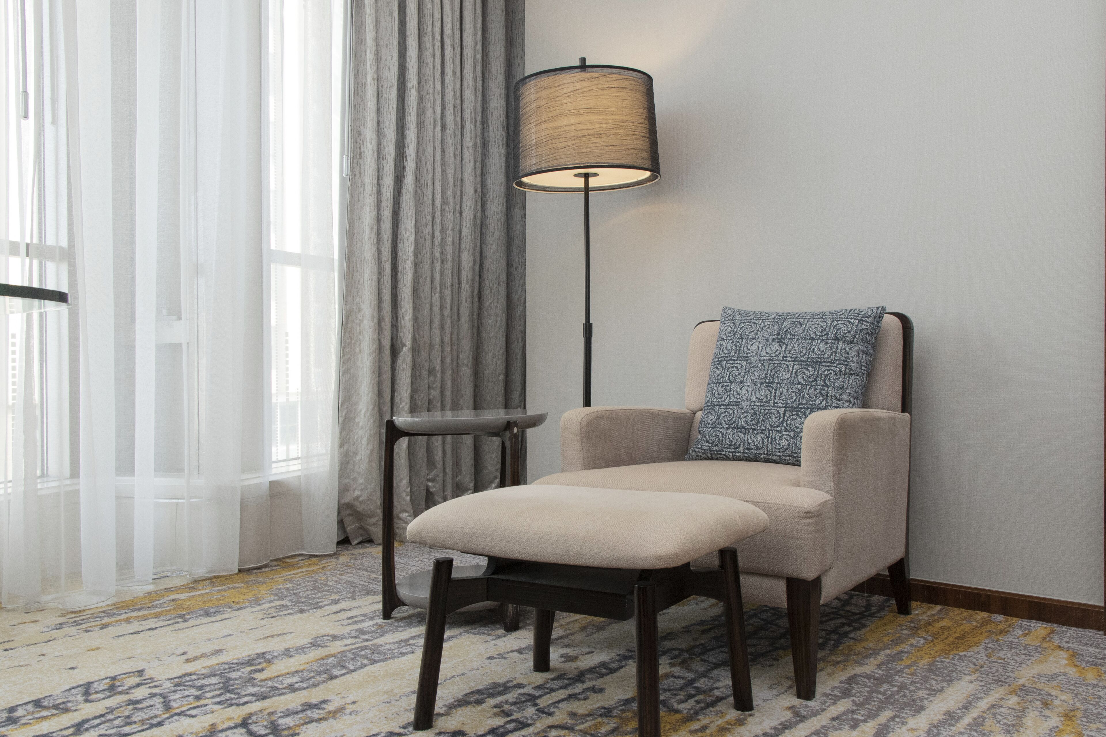 A room with a chair, a floor lamp, a small table, and a patterned carpet.