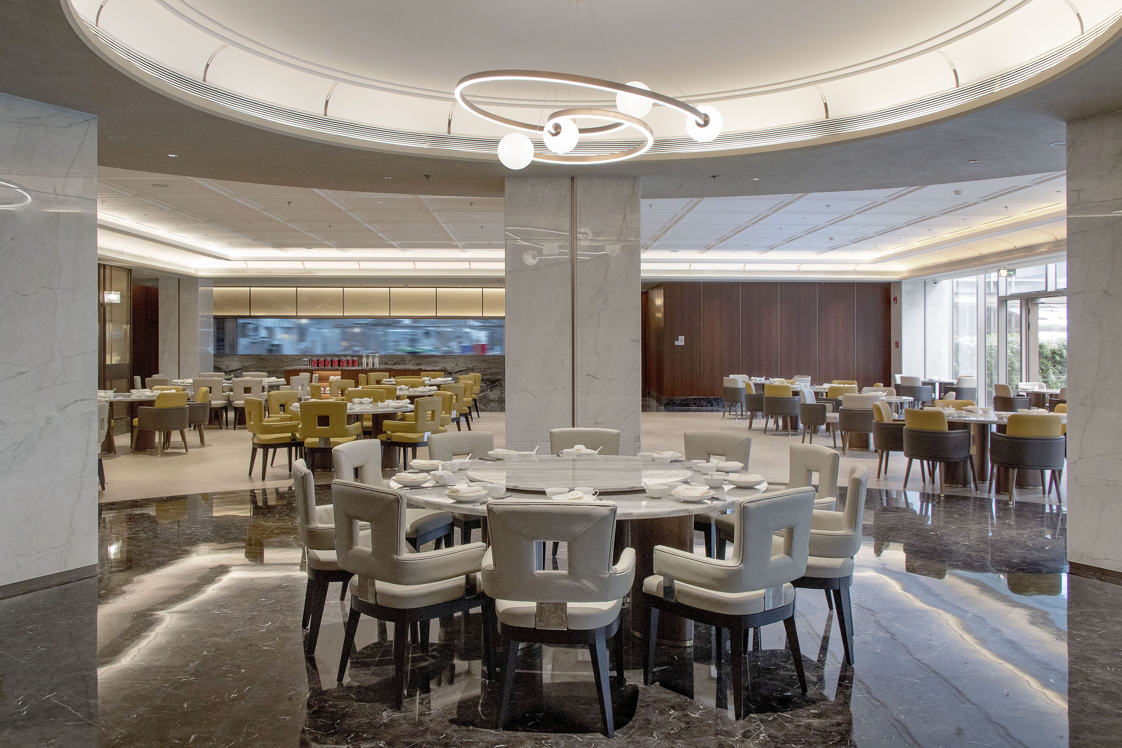 Un vaste espace dédié à la salle à manger, avec des tables et des chaises rondes, un pilier central et un grand téléviseur à écran plat en arrière-plan.