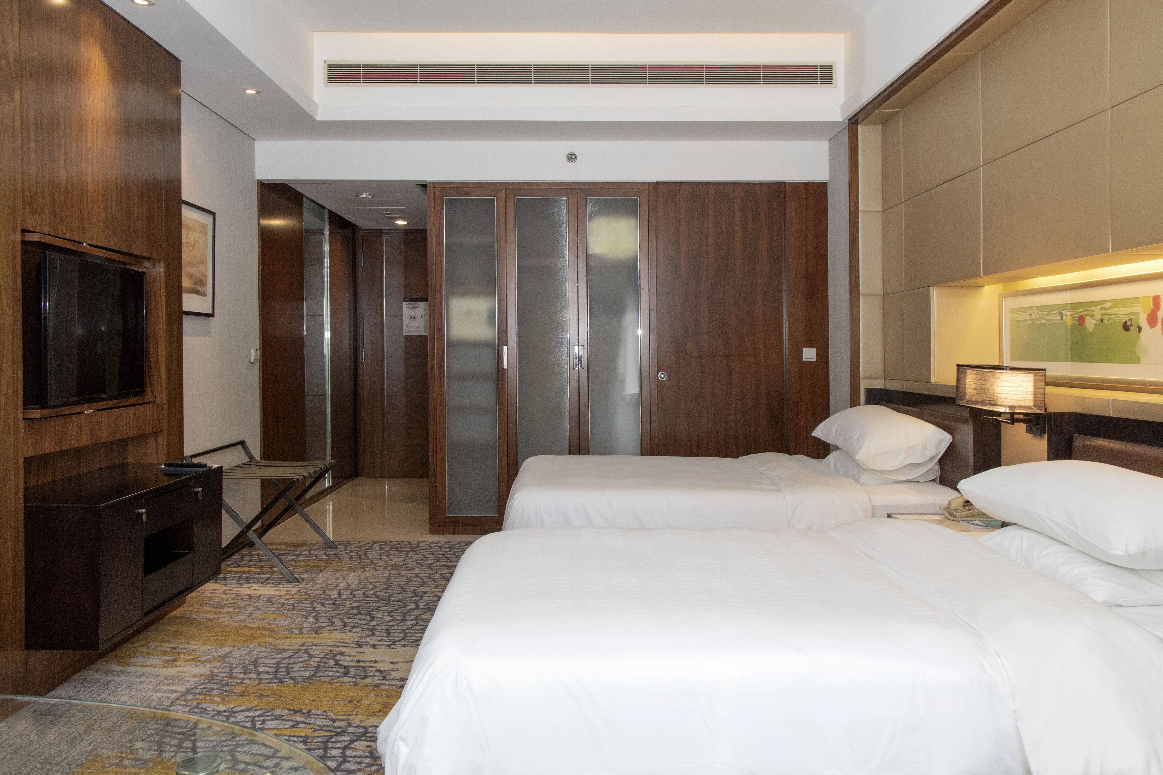 A hotel room with two beds, a TV, a wardrobe, and a desk.