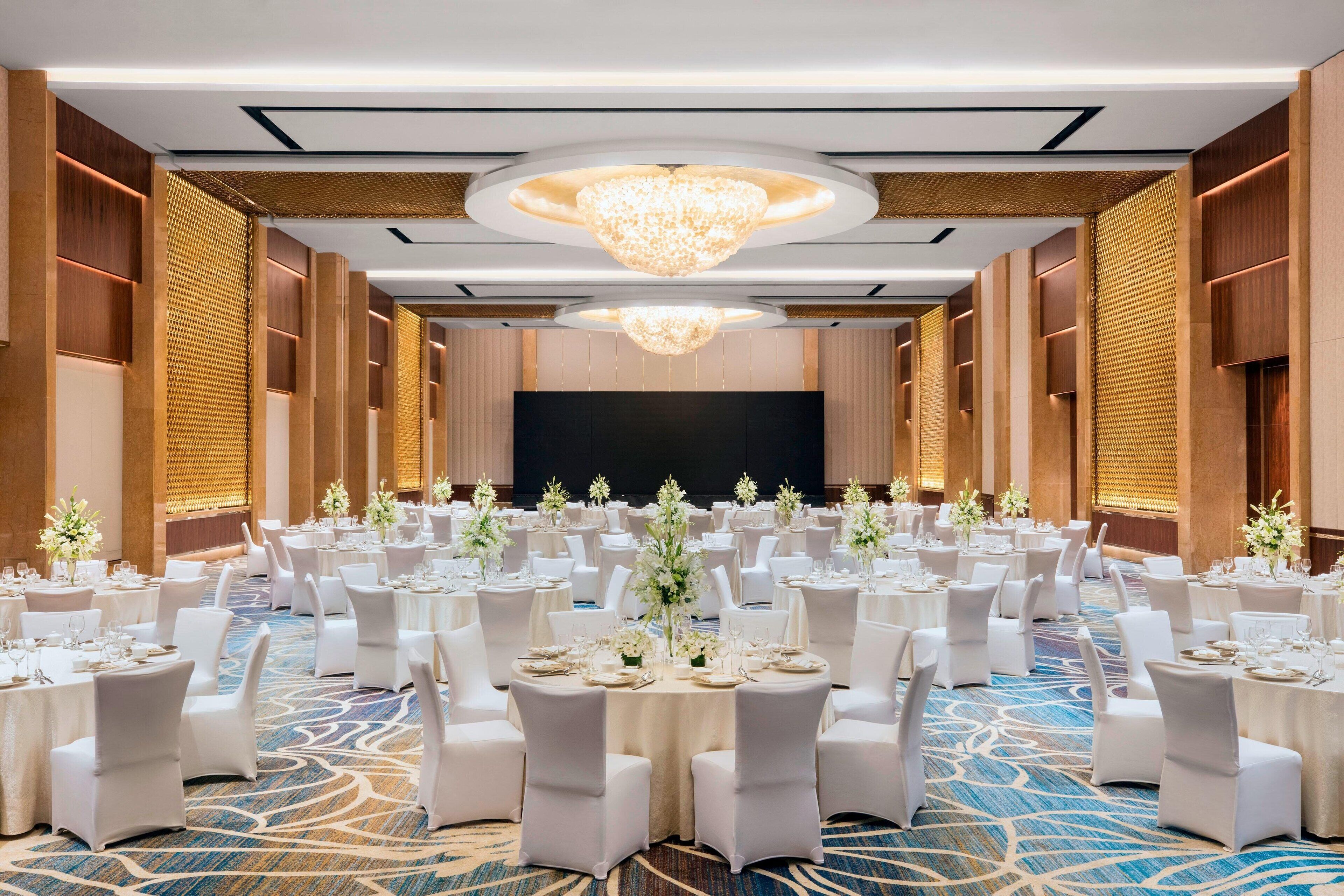 A banquet hall with round tables, white chairs, and a large screen at the front.