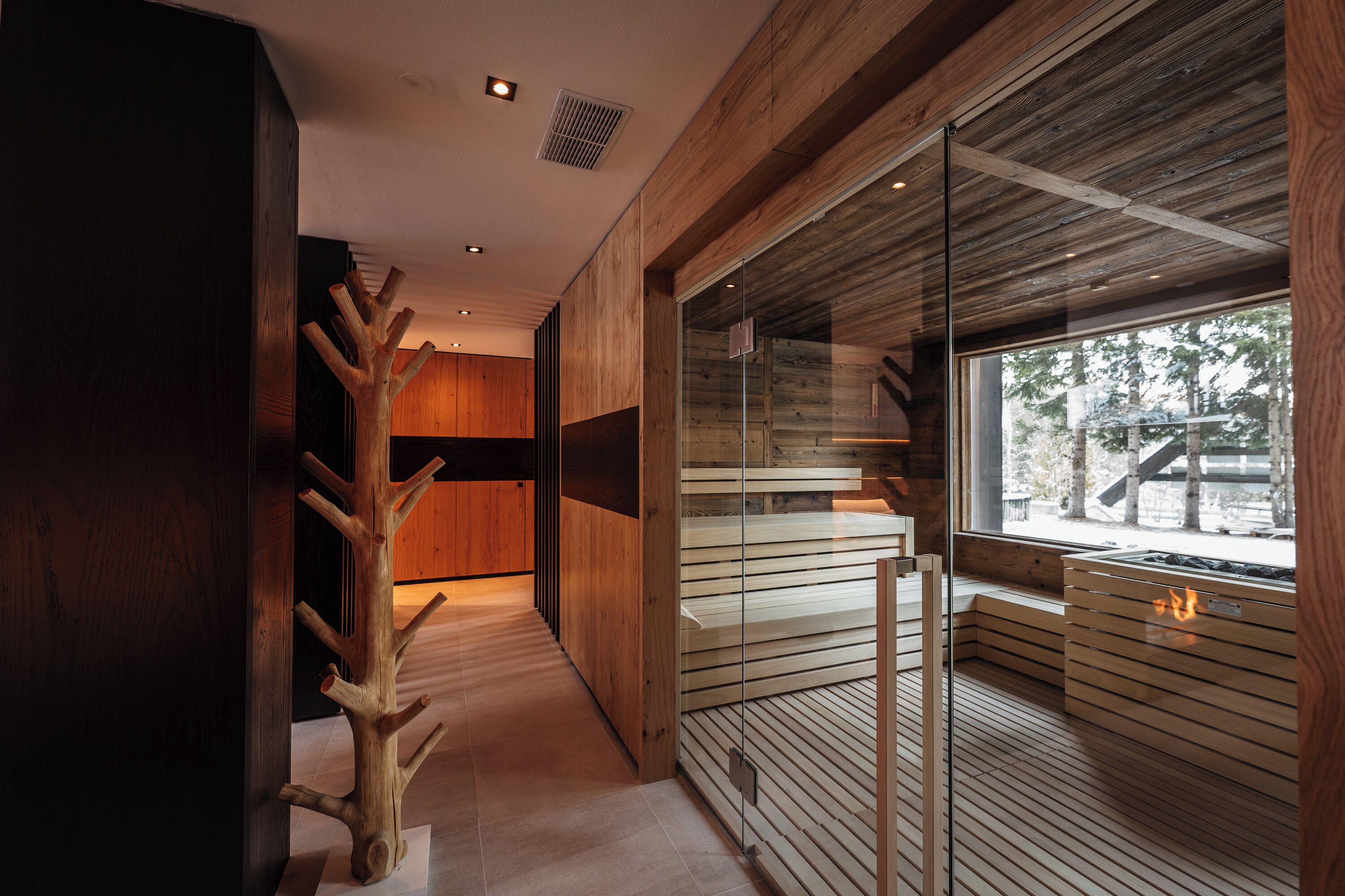 A modern interior with a wooden staircase, a glass partition, and a view of the outdoors.