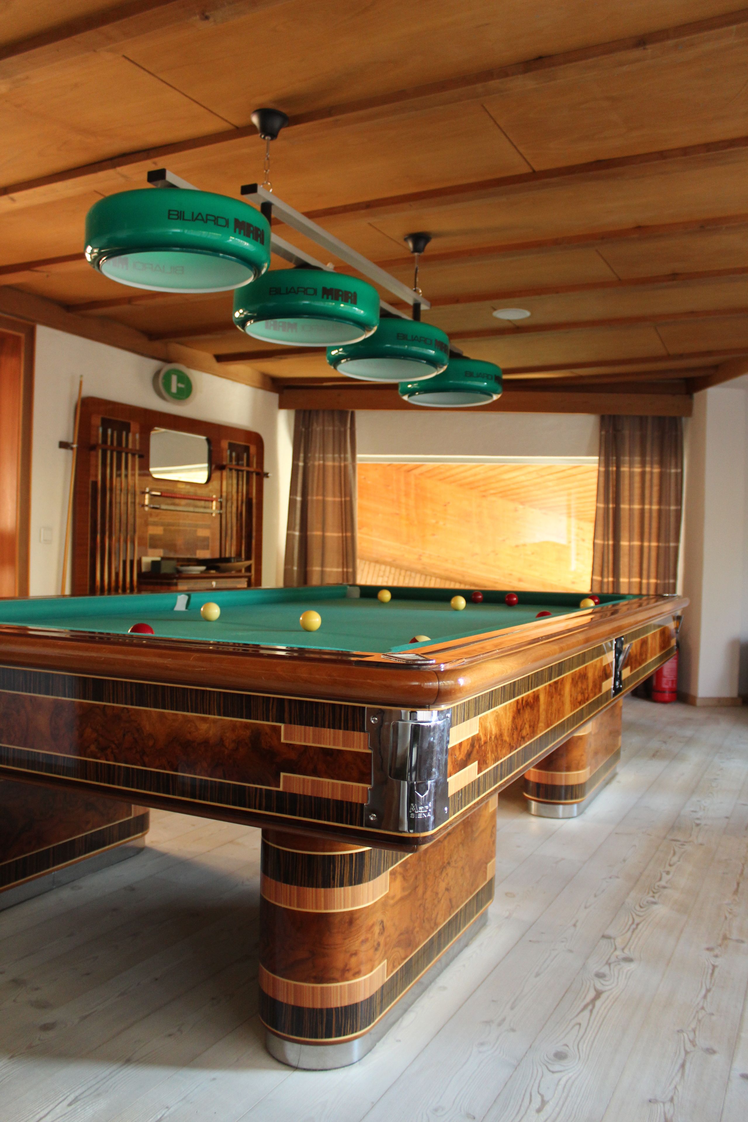 A pool table with balls, wooden beams, and hanging lights.