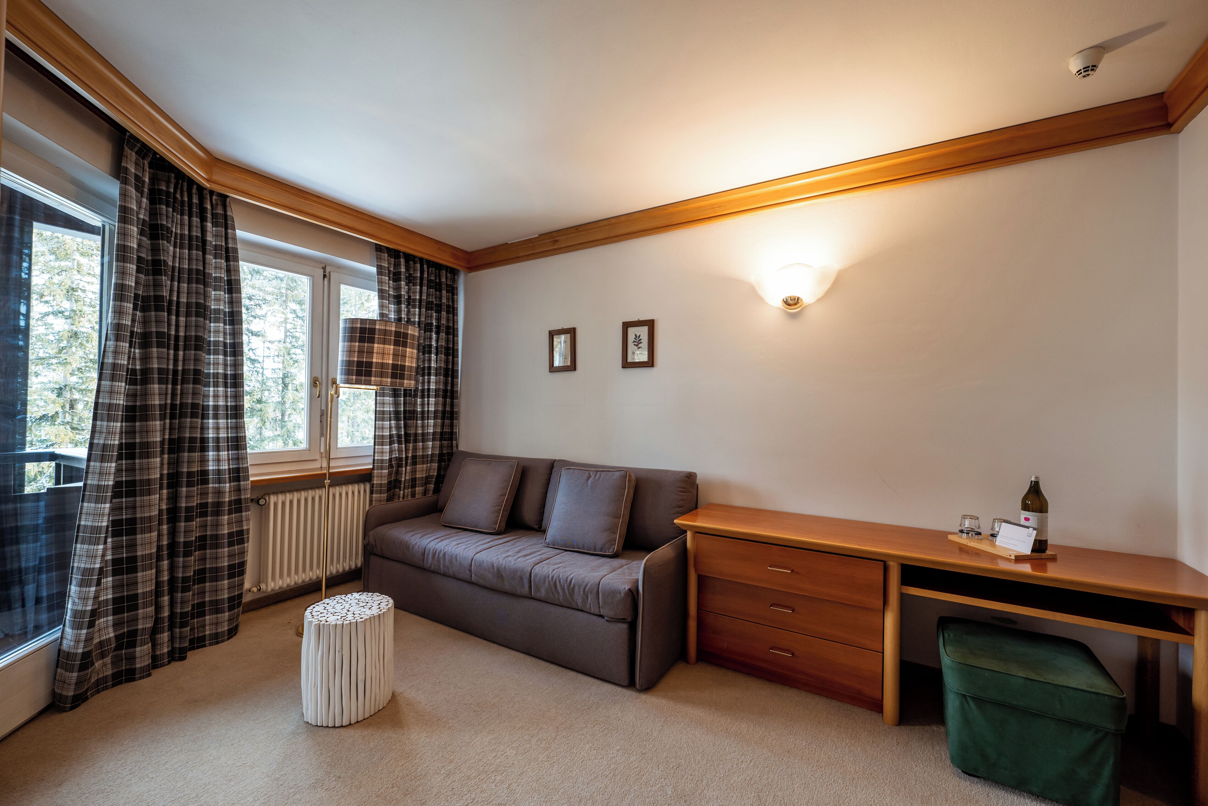A room with a sofa, a wooden desk, a radiator, and a window with curtains.