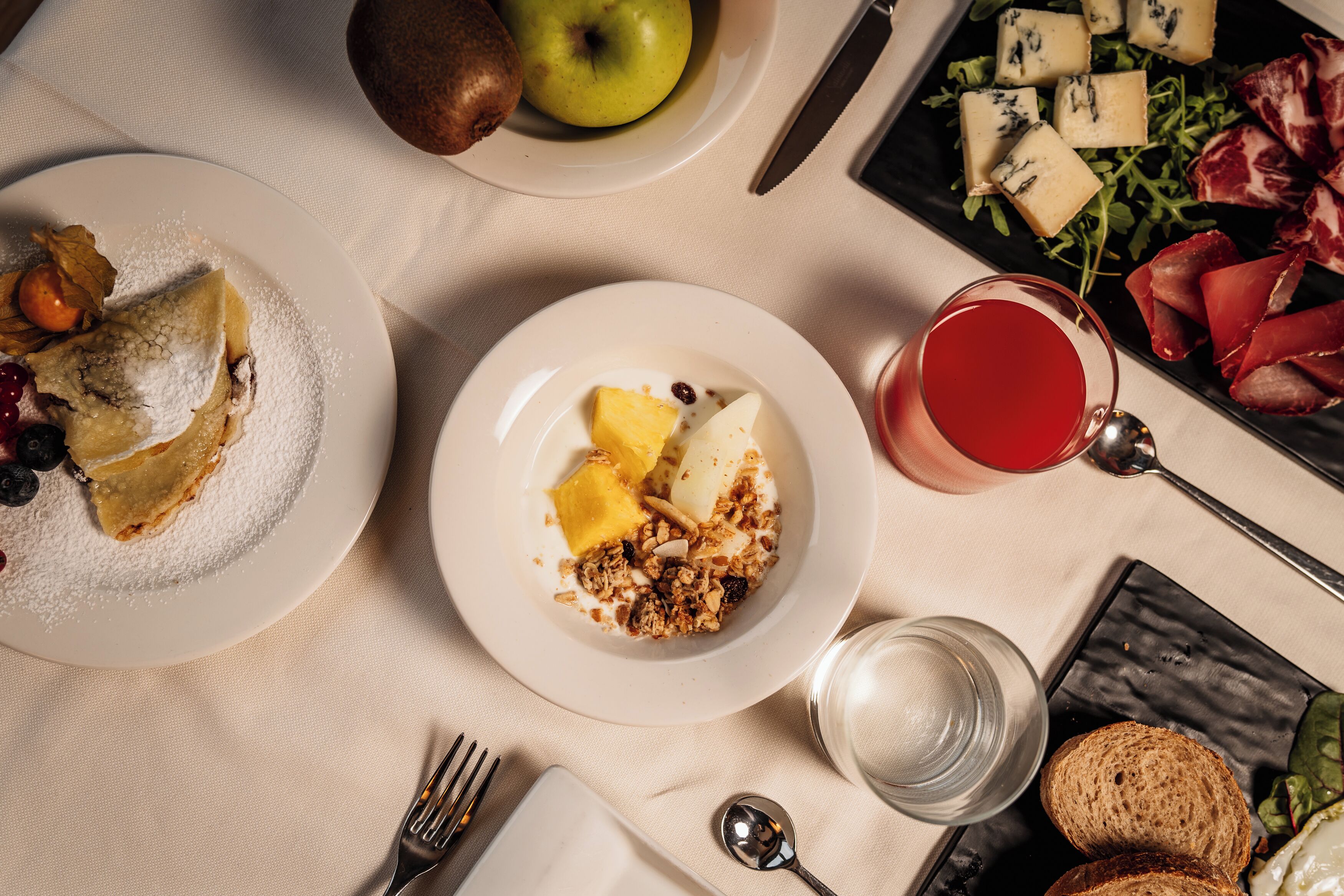 A breakfast setting with plates of food, a glass of red drink, and cutlery on a table.