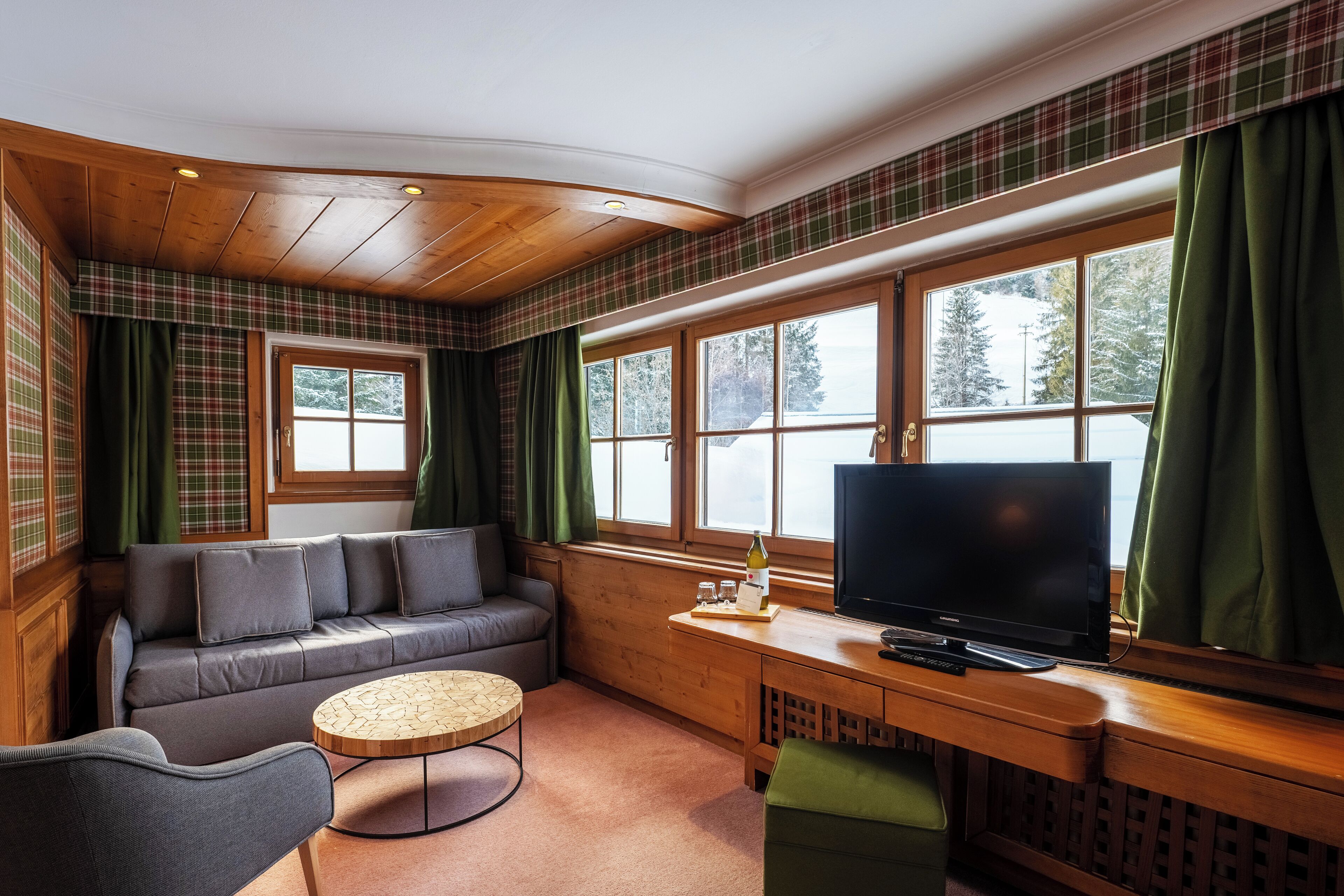A cozy room with a sofa, a small round table, a TV, and large windows with curtains.