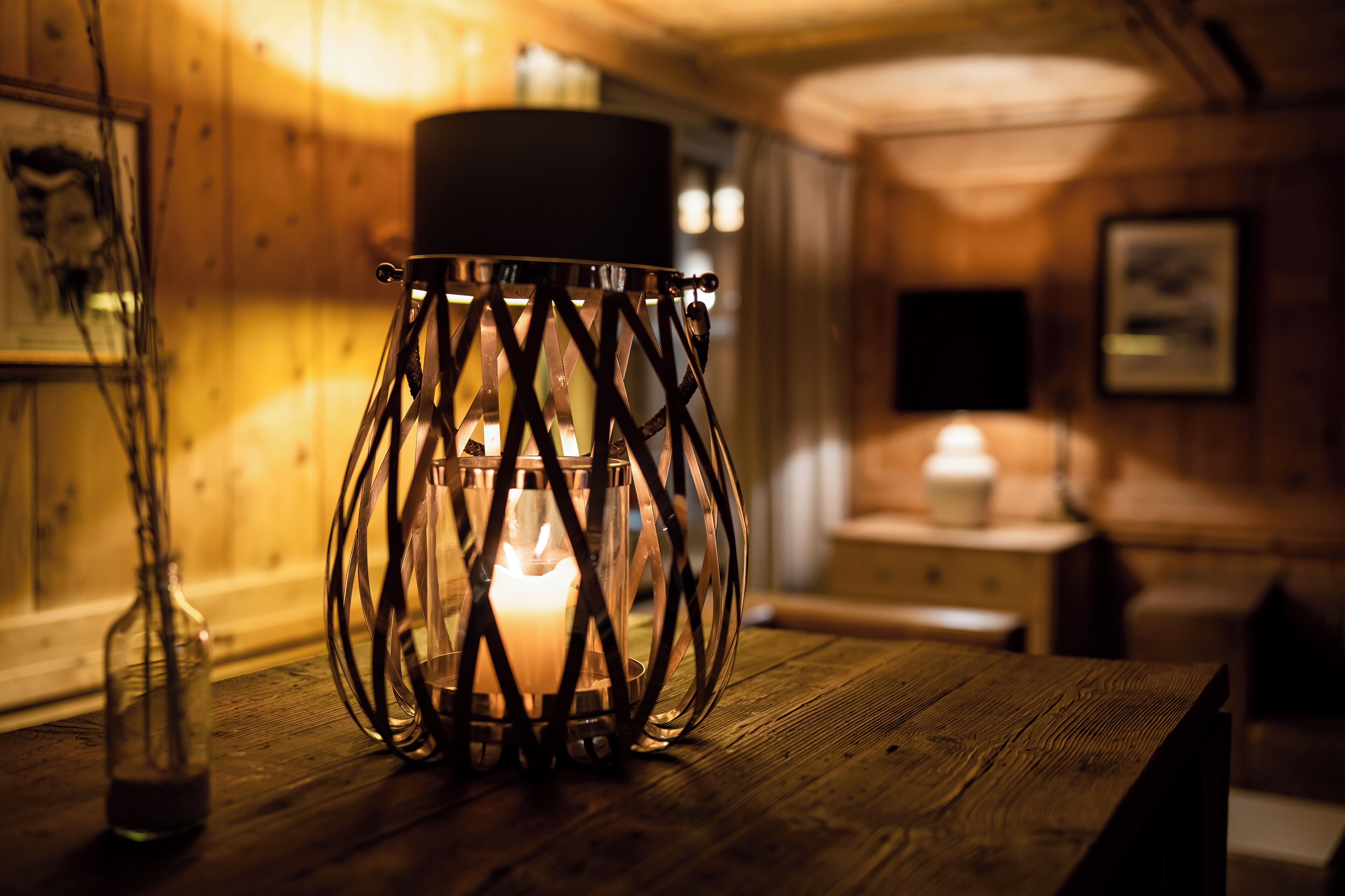 A candlelit table with a glass candle holder in a wooden room.