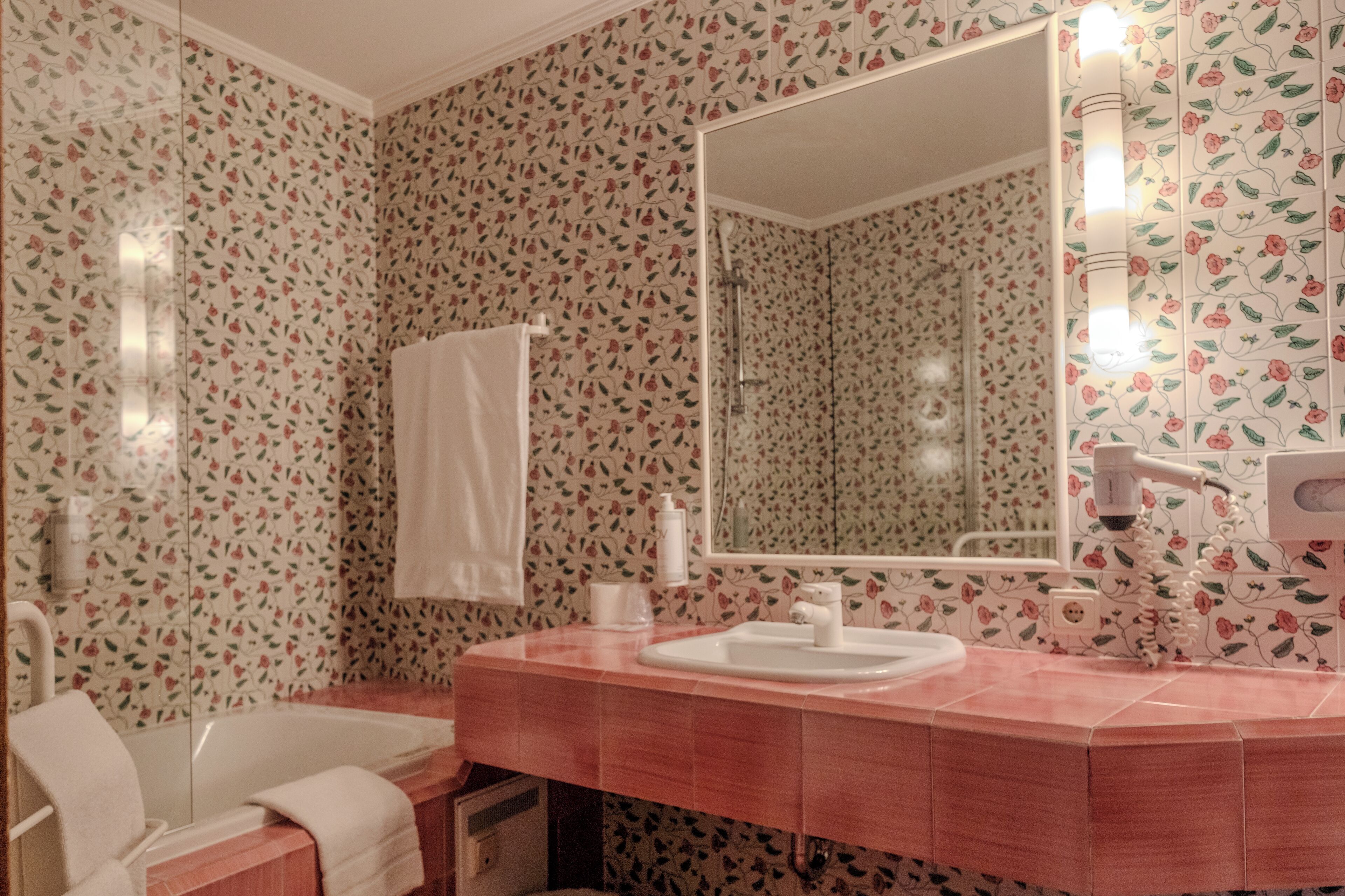 Une salle de bain avec un papier peint à motifs floraux, un lavabo blanc et un miroir.