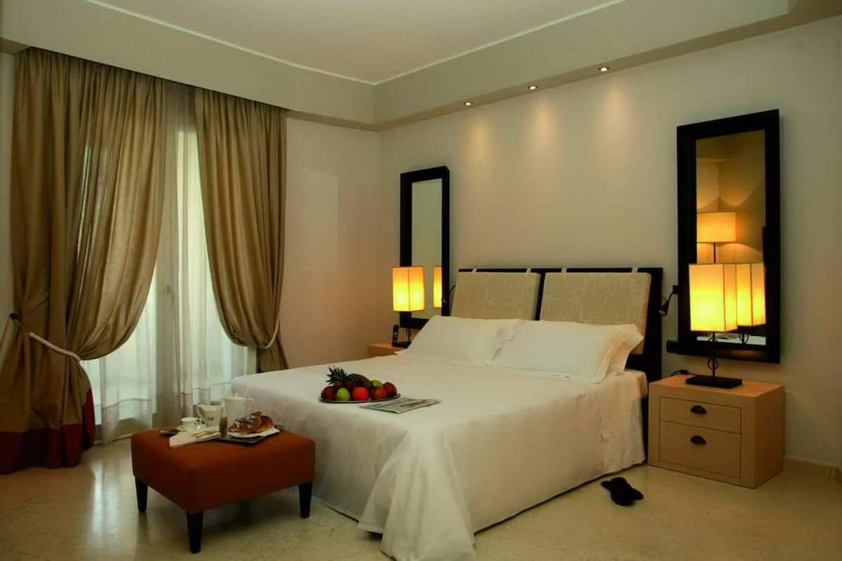 A hotel room with a bed, bedside lamps, a nightstand, a mirror, and a window with curtains.