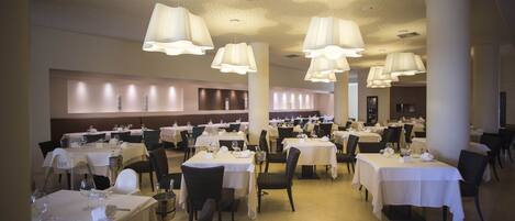 A spacious dining area with multiple tables and chairs, large hanging lamps, and a high ceiling with a decorative pattern.