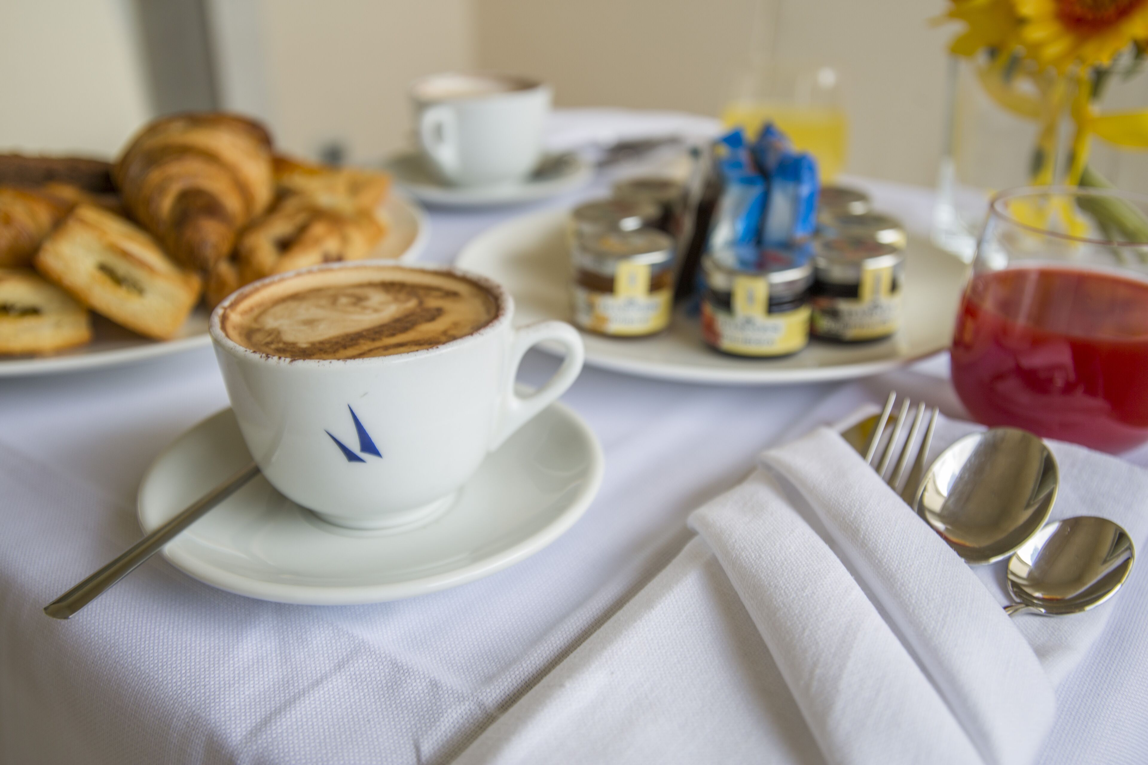 A breakfast setting with croissants, a cup of coffee, condiments, and a glass of juice on a table.