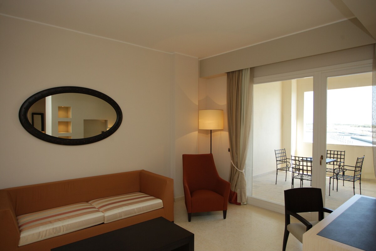 Ein Hotelzimmer mit Sofa, Sessel, Tisch, Stühlen und einem Balkon mit Blick.
