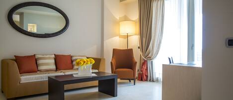 Una habitación de hotel moderna con sofá, sillón y mesa de centro con un jarrón de flores.