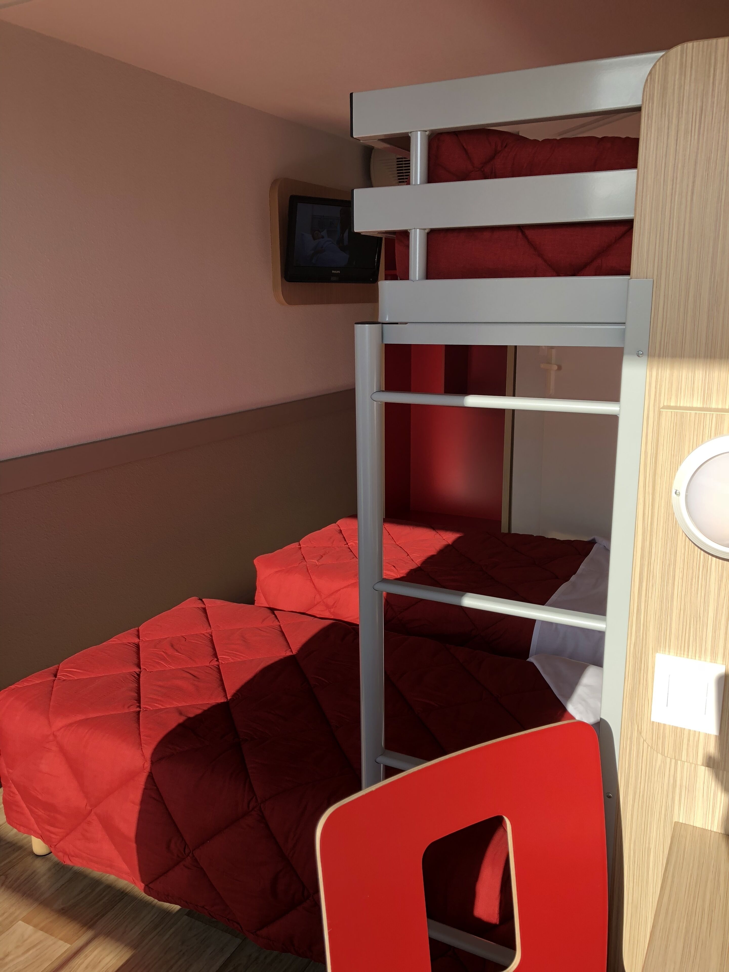 Una cama litera con ropa de cama roja, un televisor en la pared y una puerta de madera.