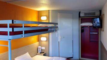Una cama individual con colchón rojo, una mesita de noche con control remoto, un armario con espejo y un televisor montado en la pared.