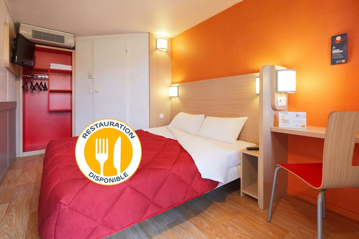 Une chambre d’hôtel équipée d’un lit, d’un bureau, d’une chaise et d’une armoire. Un panneau indique qu’un restaurant est à disposition.