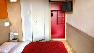 Une chambre d’hôtel avec un lit, une porte rouge, un téléviseur fixé au mur et un climatiseur mural.