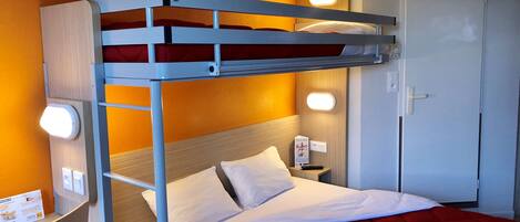 A bunk bed with white bedding and a red quilt, a bedside table with a lamp, and a door with a handle.