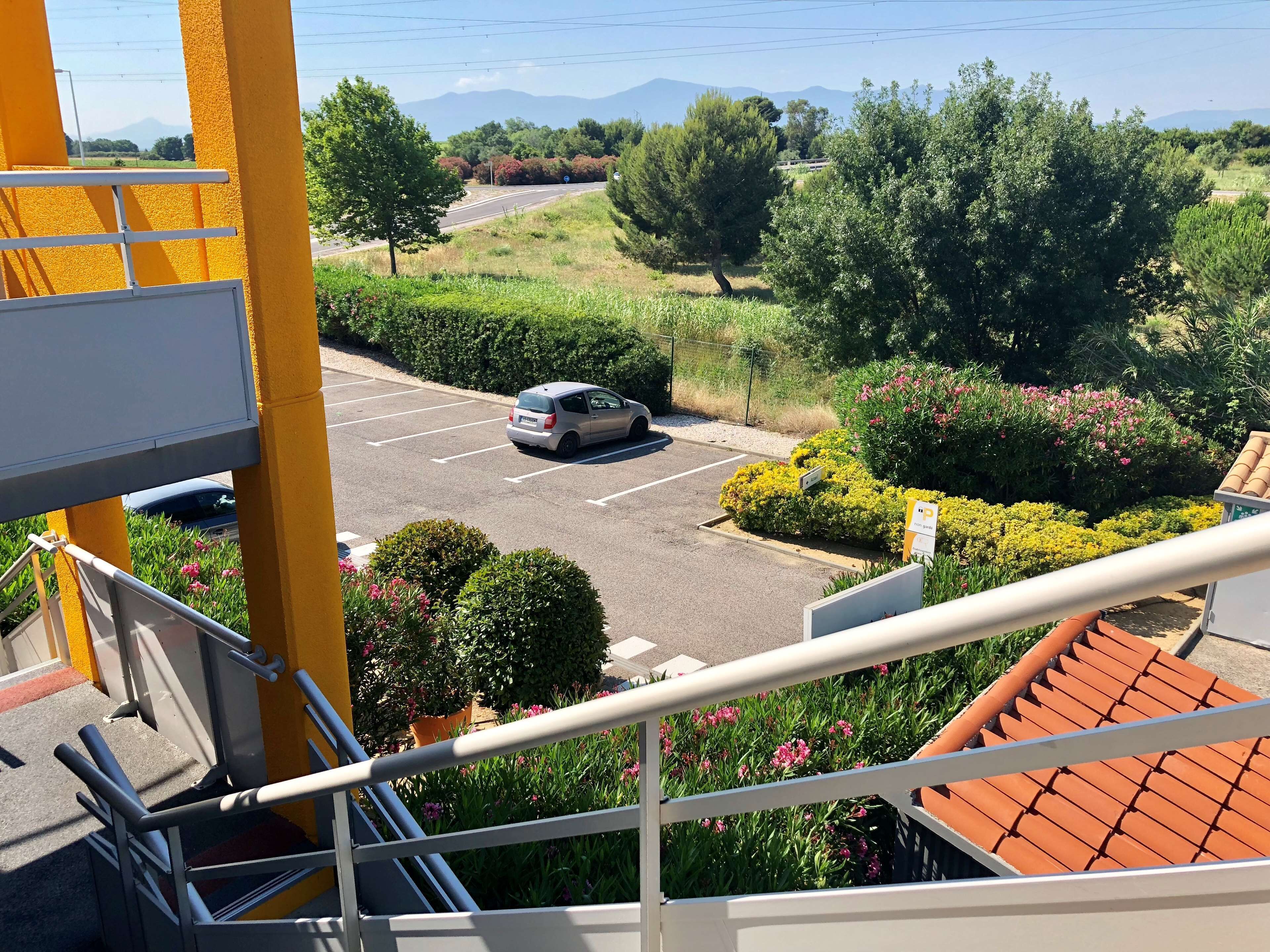 Een parkeerplaats met een auto, omringd door groen en een uitzicht op verre bergen.