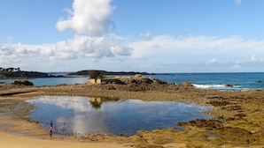 A rocky beach with a small pond, a few people, and distant hills under a clear sky. - Résidence Lagrange Vacances Les Roches Douvres (Saint-Briac-sur-Mer)
