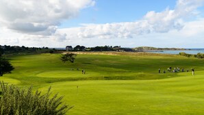 A golf course with a large house in the background, a body of water, and a clear sky. - Résidence Lagrange Vacances Les Roches Douvres (Saint-Briac-sur-Mer)