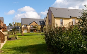 A residential area with houses featuring balconies, a well-maintained lawn, and surrounding greenery. - Résidence Lagrange Vacances Les Roches Douvres (Saint-Briac-sur-Mer)