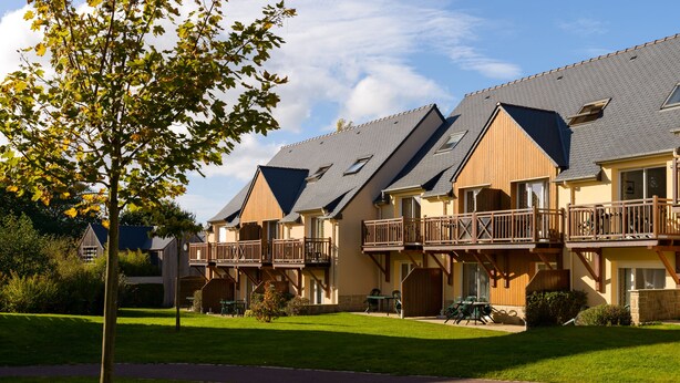 A row of two-story wooden houses with balconies, a grassy lawn, and a clear sky. - Résidence Lagrange Vacances Les Roches Douvres (Saint-Briac-sur-Mer)