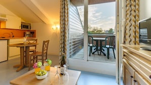 A modern kitchen with a microwave, sink, and coffee maker. There is a dining area with a table and chairs, and a balcony with a view of the sky and trees. - Résidence Lagrange Vacances Les Roches Douvres (Saint-Briac-sur-Mer)