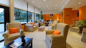 A spacious living area with multiple sofas and armchairs, large windows offering a view of greenery, and a bright, modern interior design. - Résidence Lagrange Vacances Les Roches Douvres (Saint-Briac-sur-Mer)