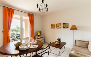 A dining area with a table set for four, a pitcher, glasses, and a bowl of fruit. There is a sofa and a lamp in the room.