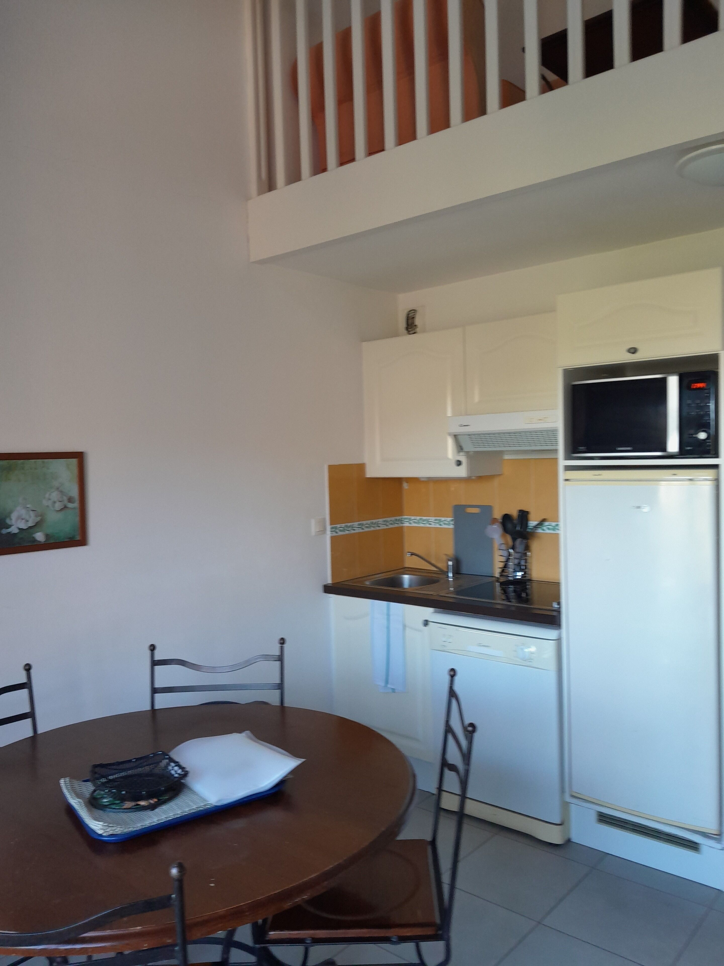 A dining area with a round table and chairs, a kitchen with a microwave and dishwasher, and a white railing.