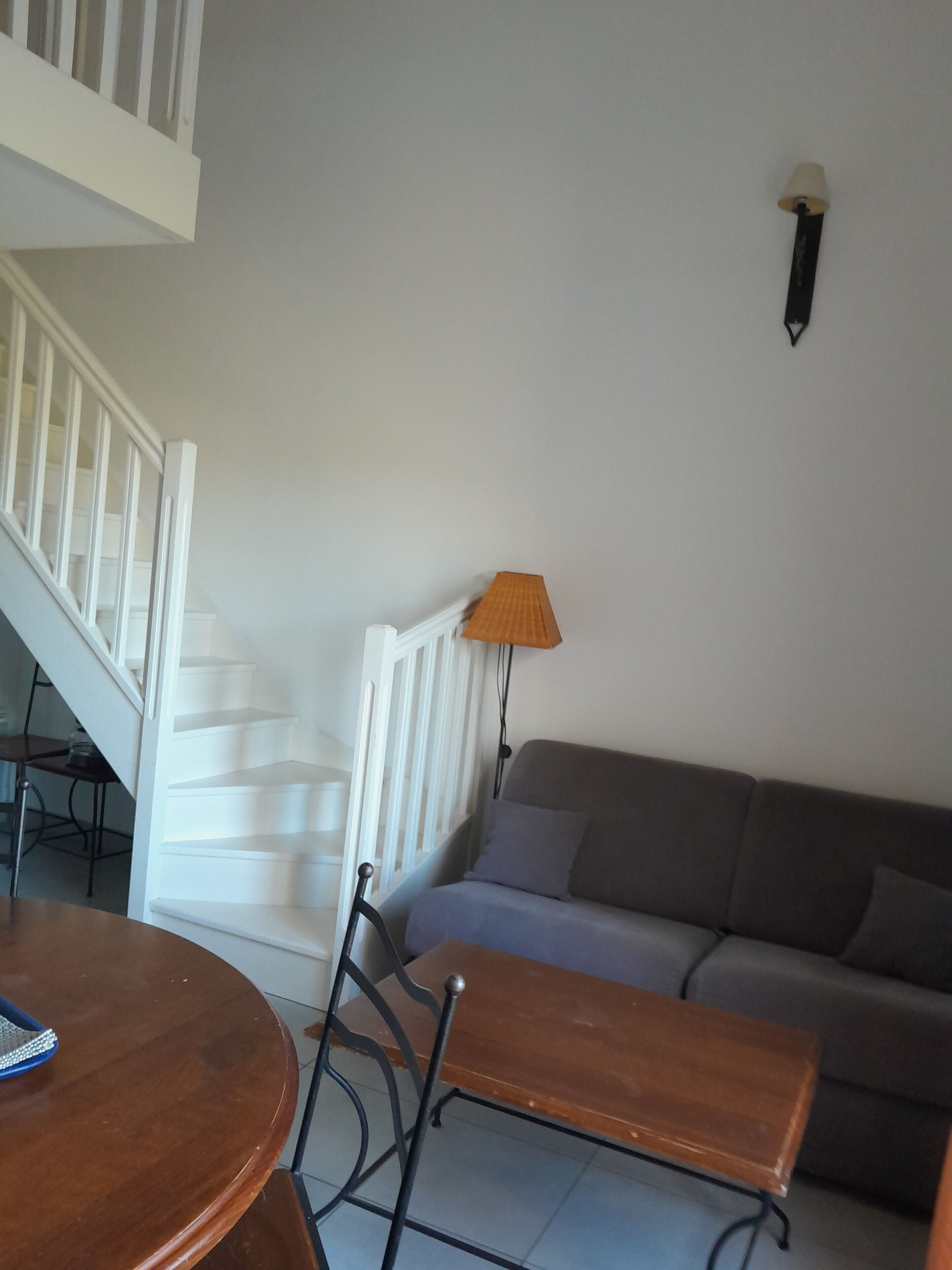A staircase with white railings, a grey sofa, a wooden table, and a lamp.