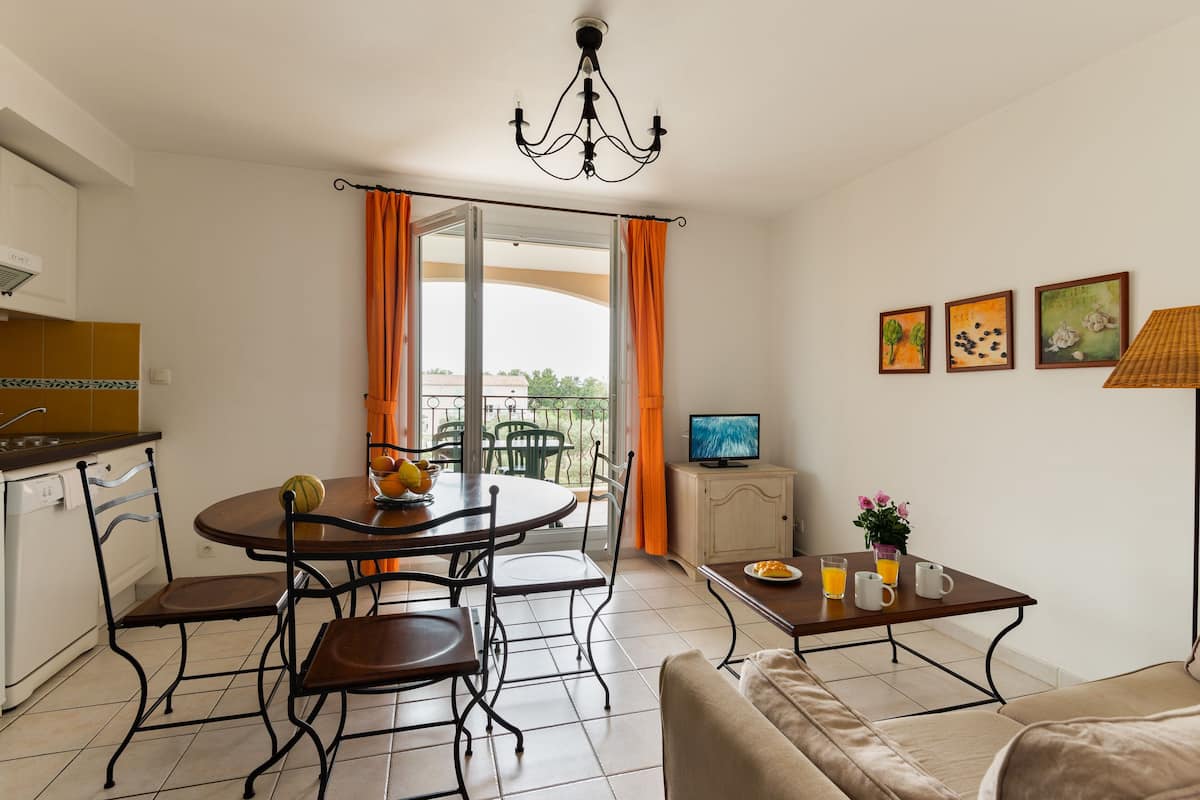 A modern living room with a dining area, a television, and a balcony with orange curtains.