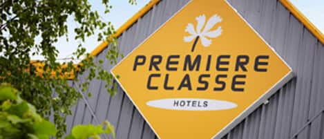 Un letrero amarillo con el texto 'PREMIERE CLASSE HOTELS' y un símbolo de hoja de arce blanca.