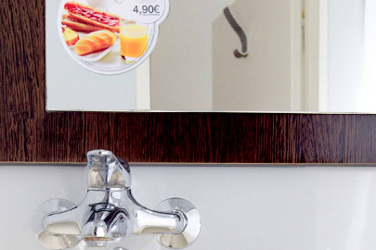 A bathroom with a modern faucet and a mirror reflecting a breakfast plate with toast and orange juice.