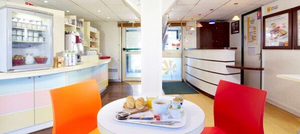 A restaurant with a counter, a refrigerator, and a table with food and drinks.