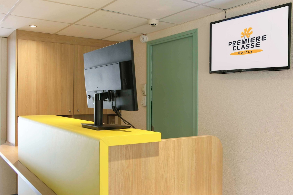 Un mostrador de recepción con un monitor de pantalla plana, una puerta verde y un cartel en la pared para Premiere Classe Hotels.